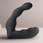 Stimulateur prostatique noir à double bras vu de profil sur fond beige, courbe flexible et embouts arrondis, design ergonomique lisse non anatomique, double moteur.