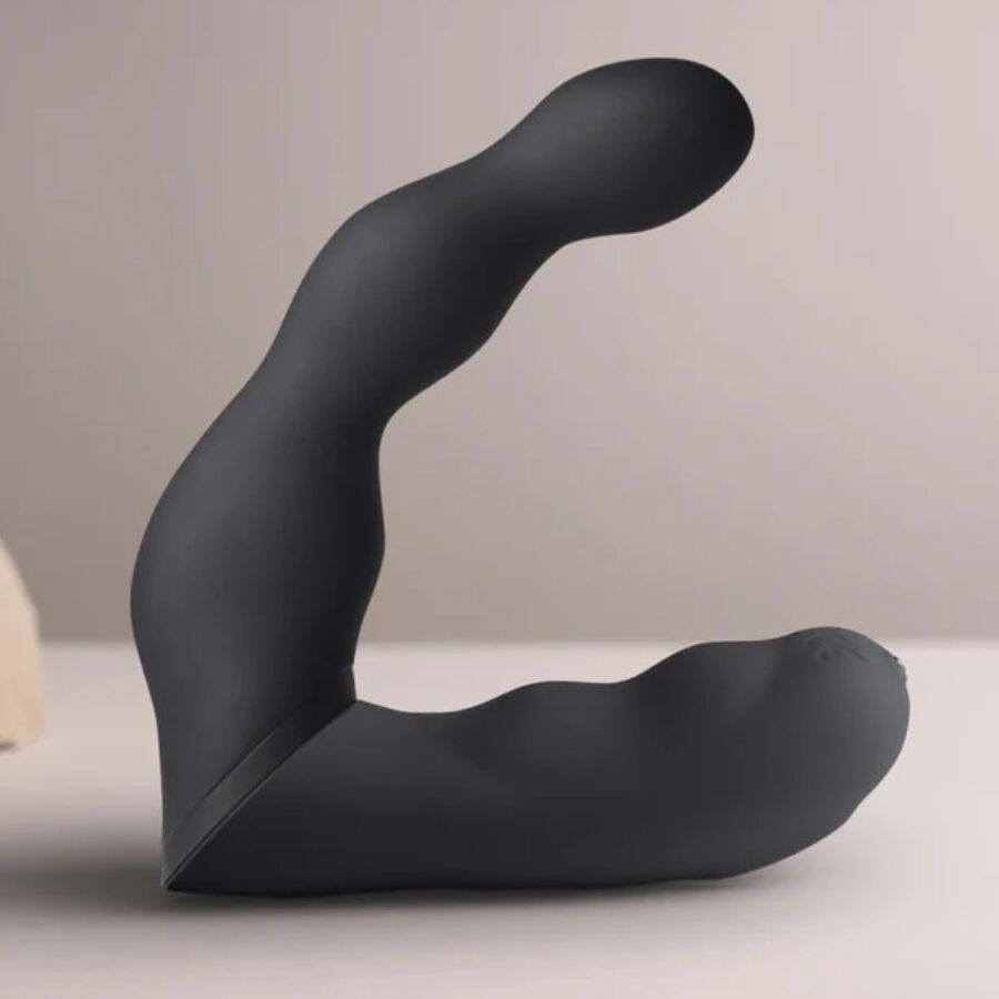 Stimulateur prostatique noir à double bras vu de profil sur fond beige, courbe flexible et embouts arrondis, design ergonomique lisse non anatomique, double moteur.