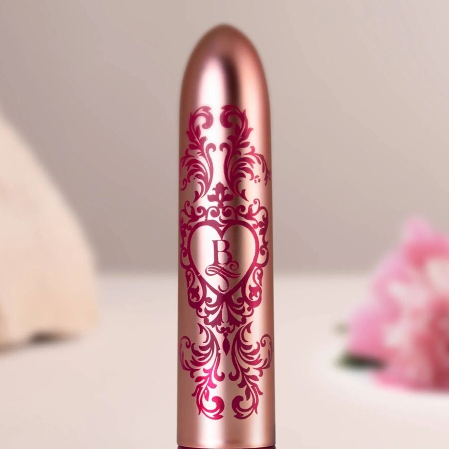 Gros plan du bullet vibrant rose doré détaillant ses arabesques bordeaux et son cœur gravé, finition baroque métallisée de ce mini vibromasseur clitoridien fin.