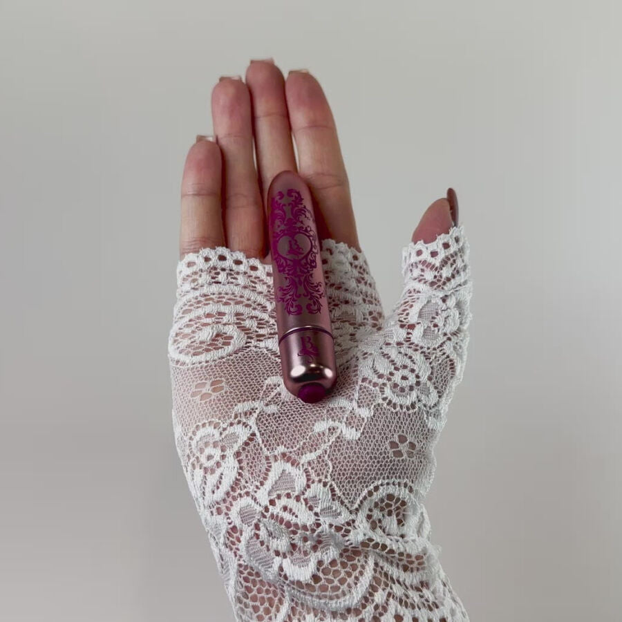 Bullet vibrant violet gravé tenu dans une main gantée de dentelle blanche, mini vibromasseur clitoridien fin à finition baroque métallisée mettant en valeur sa taille.