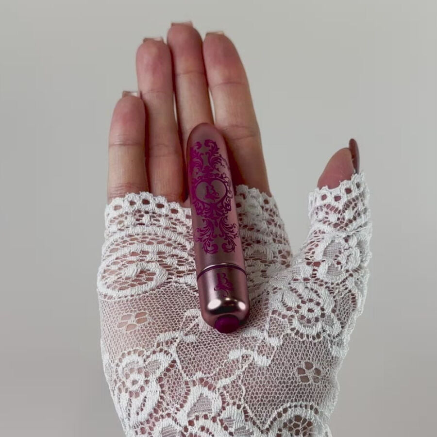 Bullet vibrant rose gravé tenu dans une main gantée de dentelle blanche, mini vibromasseur clitoridien fin mettant en valeur sa taille compacte et discrète.