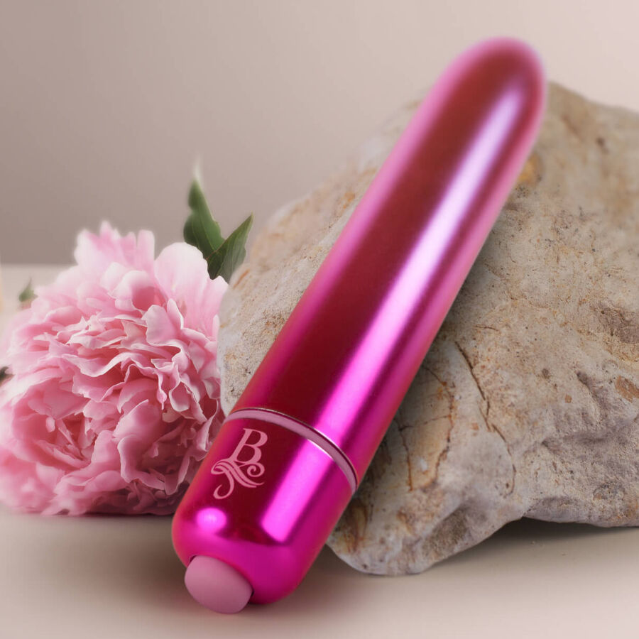 Bullet vibrant rose vif métallisé posé contre une pierre avec une fleur rose, embout de commande visible, mini vibromasseur clitoridien rechargeable Rocks-Off.