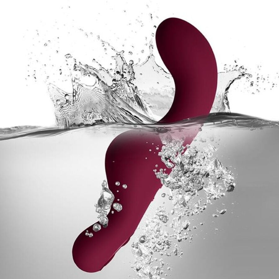 Vibromasseur à chevaucher bordeaux saisi dans une gerbe d'éclaboussures d'eau, base ondulée immergée, illustrant l'étanchéité du jouet en silicone lisse.