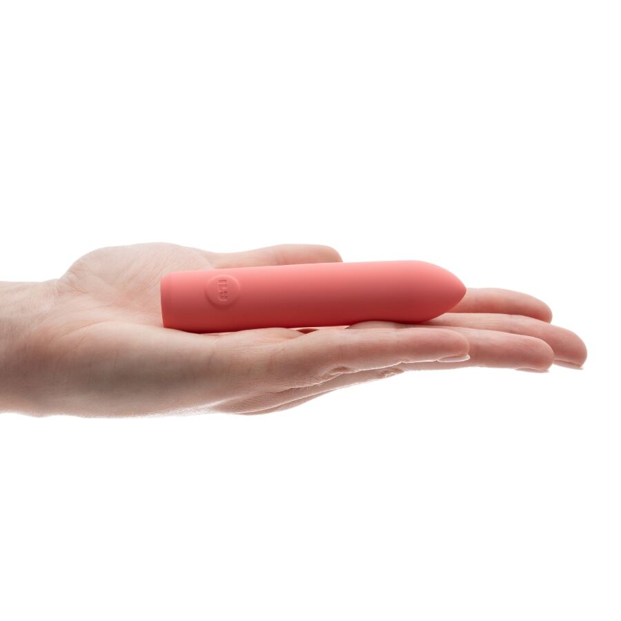 Mini bullet corail posé en travers de doigts ouverts, fin cylindre lisse présenté à plat dans la main, plan illustrant la taille de poche du produit sur fond blanc parfaitement épuré.