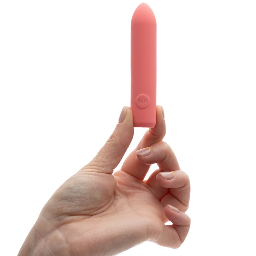 Mini bullet corail tenu verticalement entre deux doigts, cylindre lisse pointé vers le haut, démonstration du format compact et discret du produit sur fond blanc parfaitement épuré.