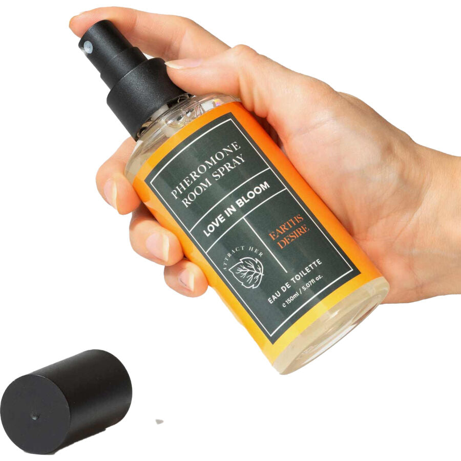 Spray d'ambiance aux phéromones Earth's Desire tenu en main, flacon ambre Pheromone Room Spray Love In Bloom et son bouchon noir, brume boisee neutralisant les odeurs.