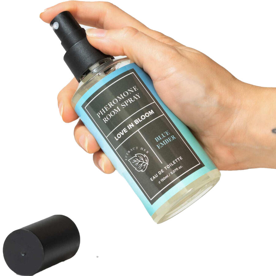 Spray d'ambiance aux phéromones Blue Ember tenu en main, flacon bleu Pheromone Room Spray Love In Bloom et bouchon noir, brume fraiche aromatique pour ambiance romantique.