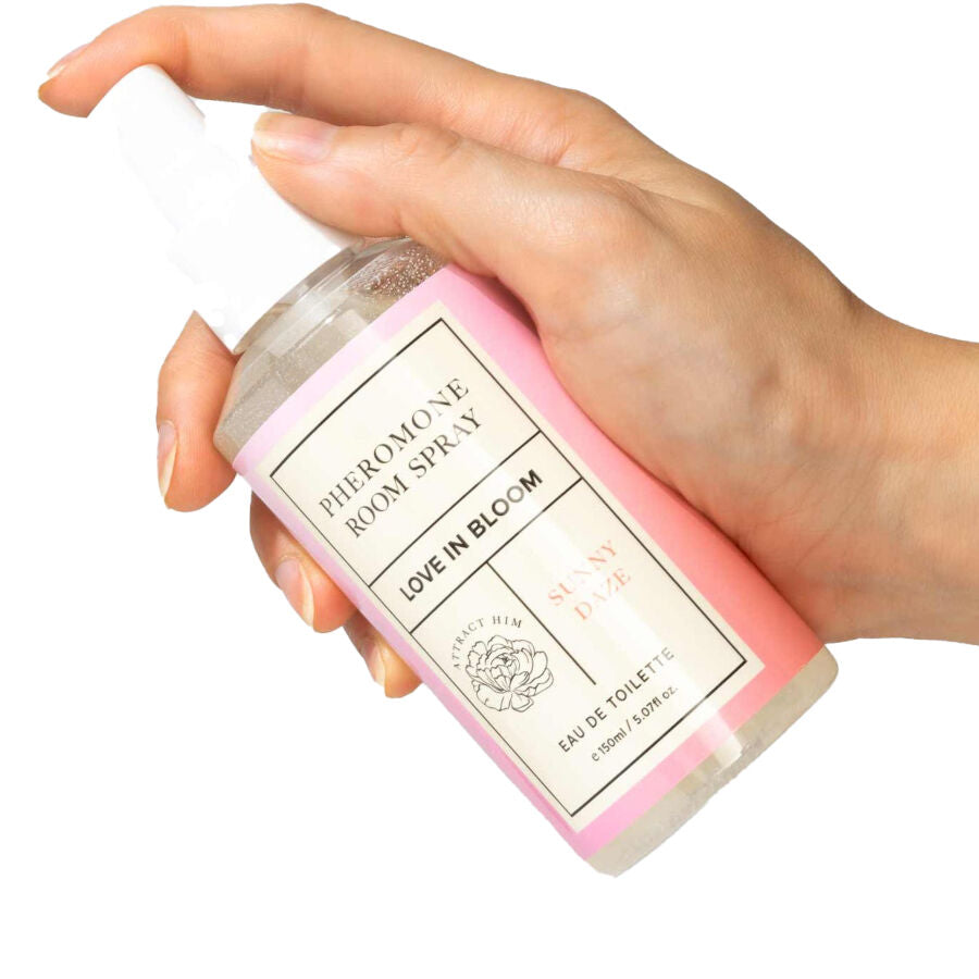Spray d'ambiance aux phéromones Sunny Daze tenu en main, flacon rose Pheromone Room Spray Love In Bloom vaporise, brume lumineuse florale qui neutralise les odeurs.
