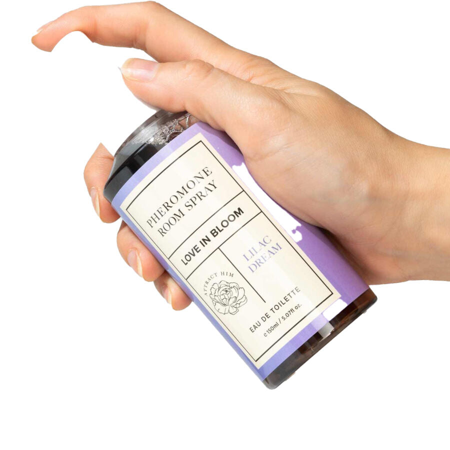 Spray d'ambiance aux phéromones Lilac Dream tenu en main, flacon violet Pheromone Room Spray Love In Bloom, brume douce vanille musc pour une atmosphere relaxante Eye Of Love.