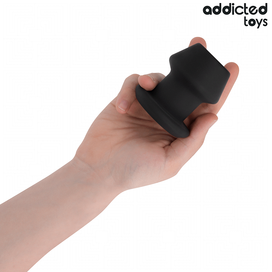Plug anal creux tunnel Addicted en silicone noir tenu en main, forme champignon a base evasee, soulignant le volume genereux du modele extreme.