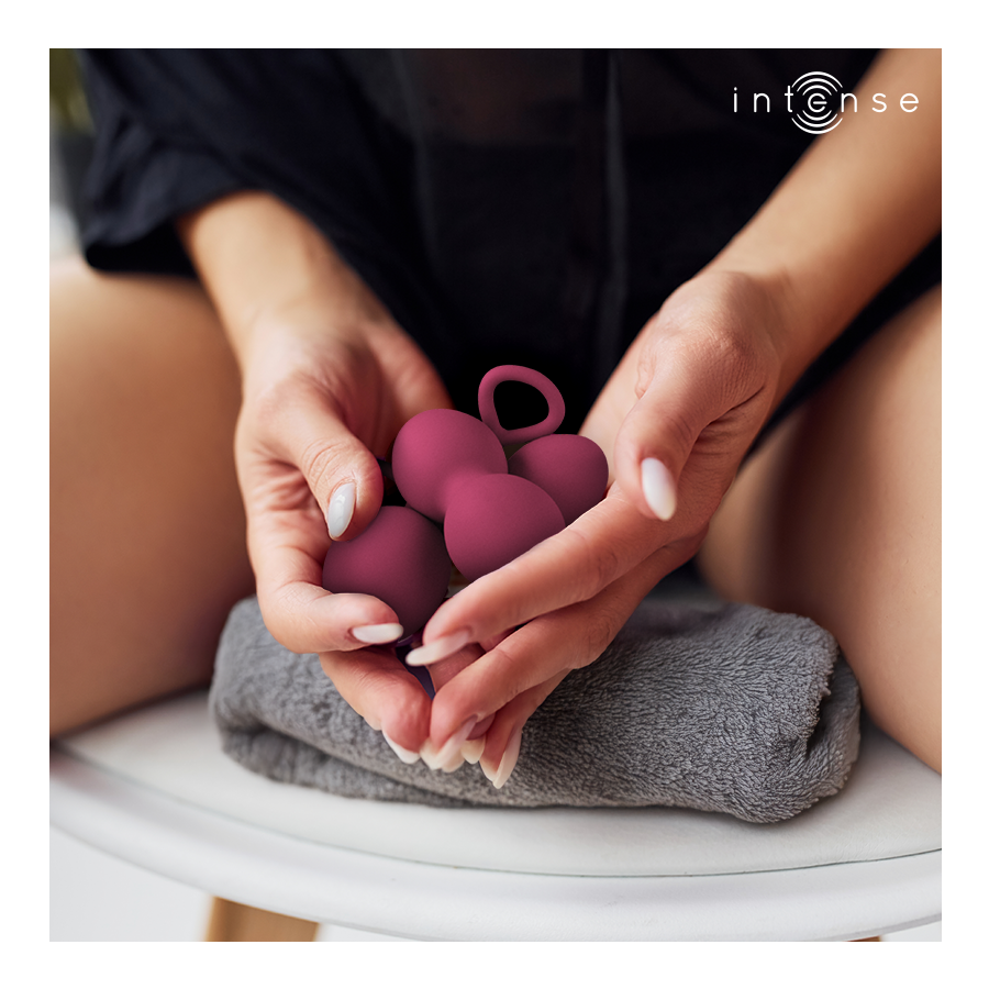 Boules de Kegel Charli bordeaux en silicone tenues au creux des mains au-dessus d'une serviette, double bille a anneau, entrainement du plancher pelvien