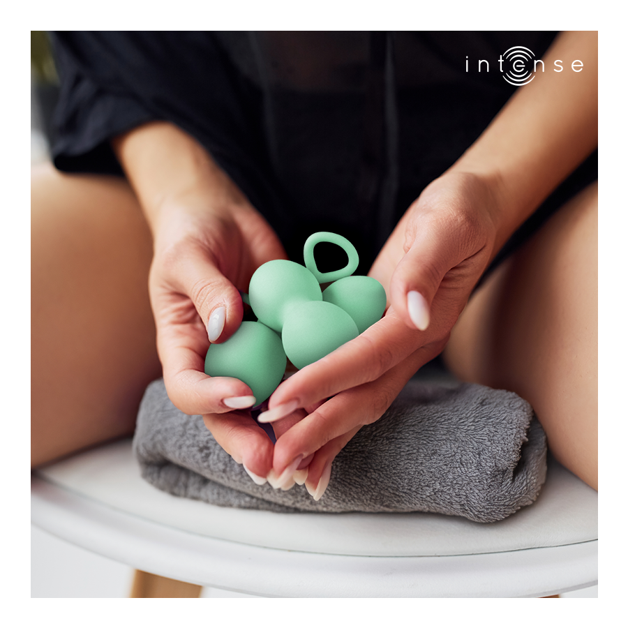 Boules de Kegel Charli vert d'eau en silicone tenues au creux des mains au-dessus d'une serviette, double bille a anneau, entrainement du plancher pelvien