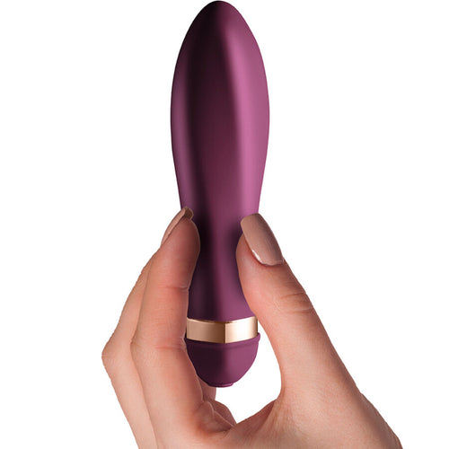 Vibromasseur classique du coffret Dare tenu entre les doigts, gros plan sur la pointe arrondie prune et la bague doree, silicone doux a 10 vibrations etanche.