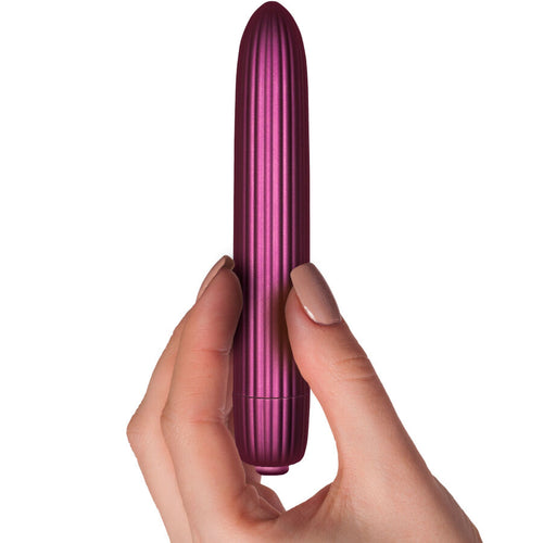 Mini vibromasseur nervure Hera tenu entre les doigts, gros plan sur les stries metallisees prune et le format discret allonge, 10 niveaux d'intensite.