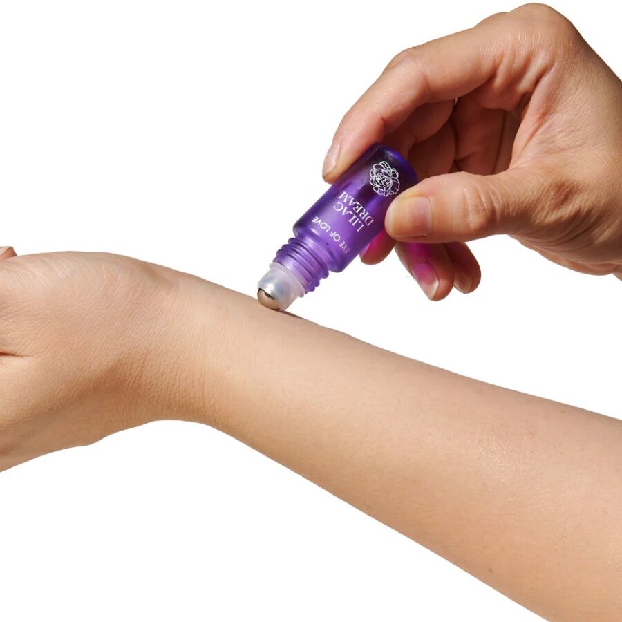 Application du parfum roll-on aux phéromones Lilac Dream sur l'avant-bras, bille violette qui glisse la fragrance vanille musc du coffret duo femme Eye Of Love.