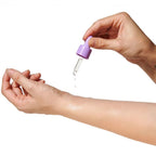 Application de l'huile de parfum aux phéromones Lilac Dream a la pipette violette sur l'avant-bras, goutte deposee sur la peau, fragrance vanille musc Eye Of Love.