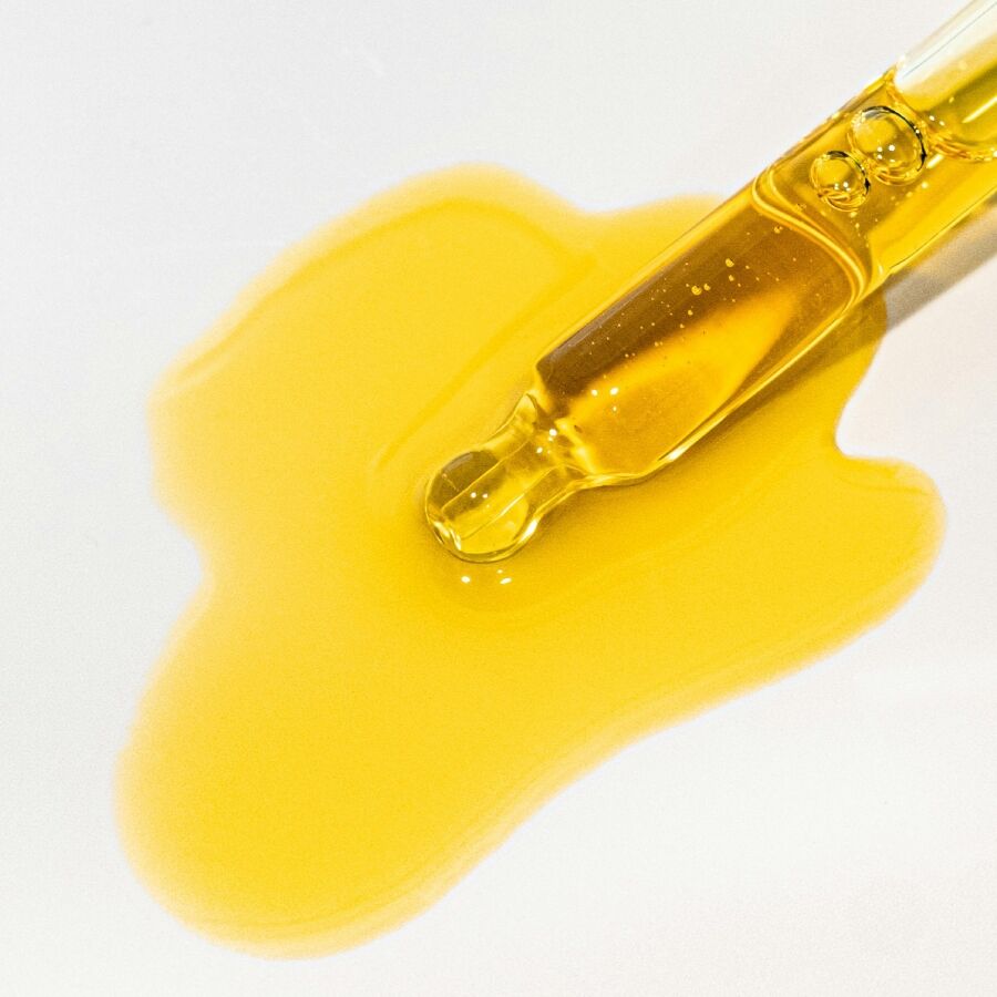 Pipette doree versant l'huile anale apaisante Slow Sex Bijoux Indiscrets sur fond clair, texture fluide et brillante mettant en avant la glisse de ce soin intime aux extraits vegetaux