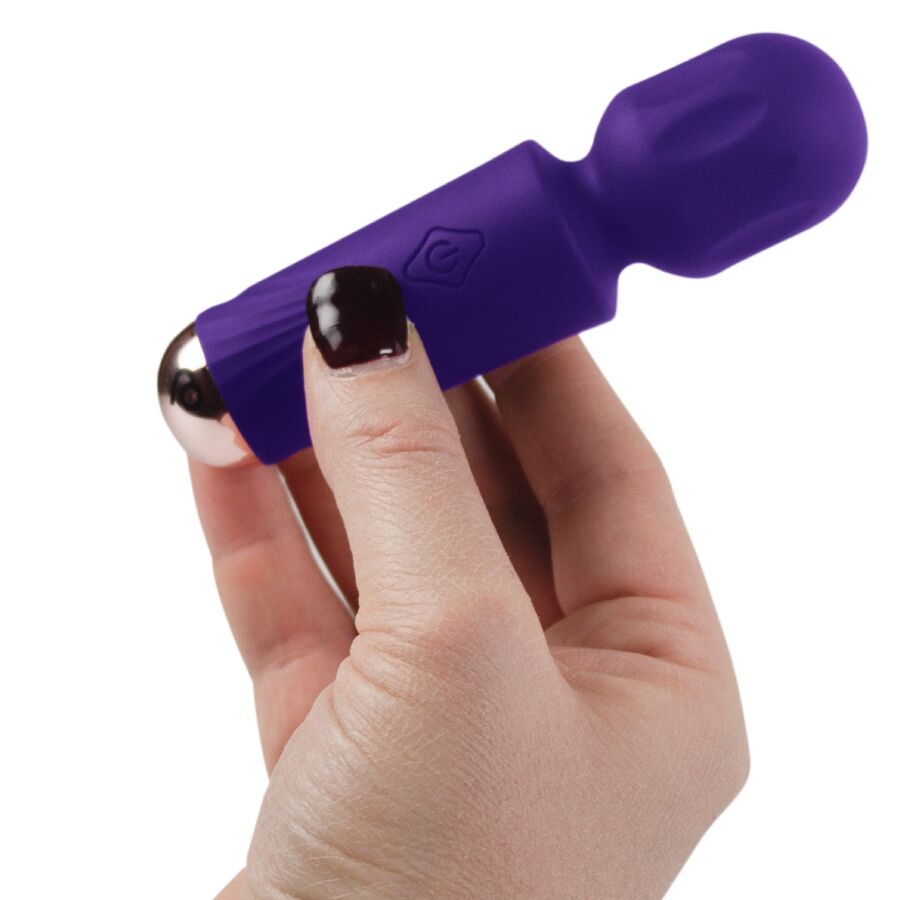 Mini wand vibrant violet tenu entre deux doigts d'une main aux ongles vernis, illustrant le format poche très compact de ce vibromasseur rechargeable 16 fonctions.