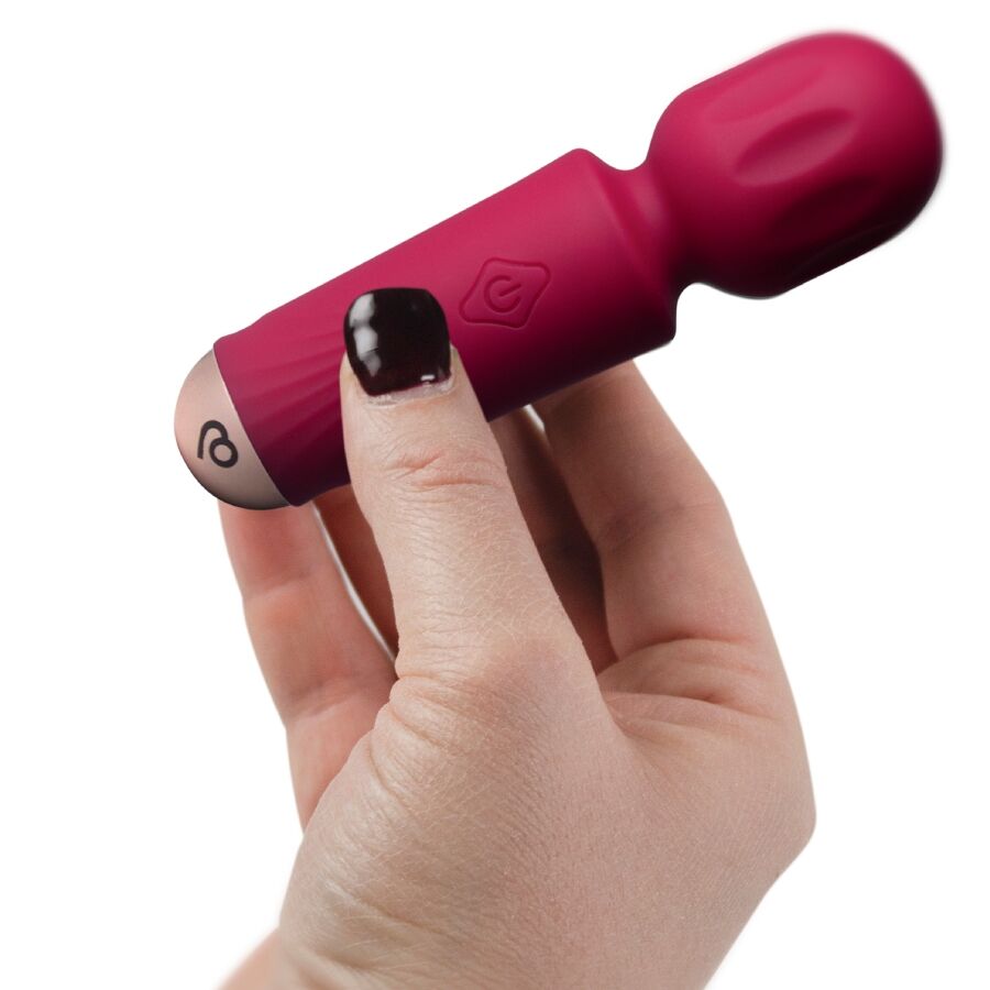 Mini wand vibrant rose foncé tenu entre deux doigts aux ongles vernis foncés, mettant en valeur le format ultra-compact de ce vibromasseur rechargeable 16 fonctions.