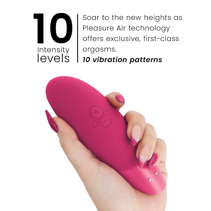 Main tenant le stimulateur clitoridien framboise Womanizer Enhance de profil près du visuel '10 intensity levels' : embout d'aspiration et boutons +/- en silicone.