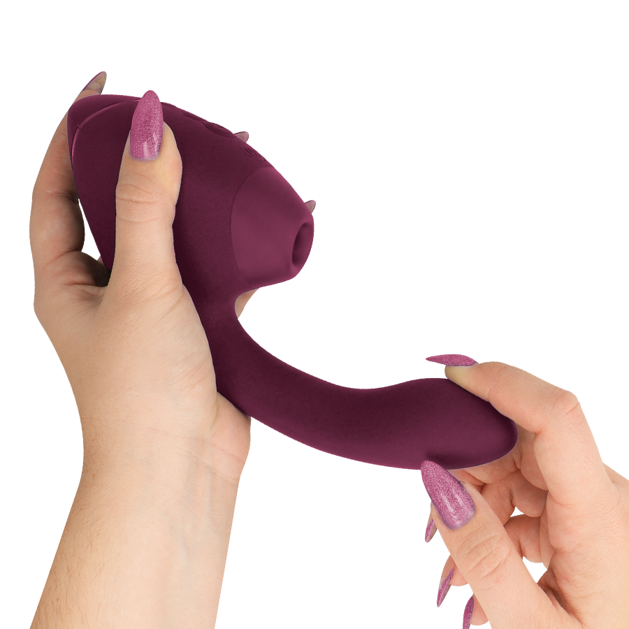 Stimulateur double bordeaux Womanizer tenu entre deux mains, embout de succion orienté vers le haut et bras vibrant interne lisse, surface silicone sans anatomie.