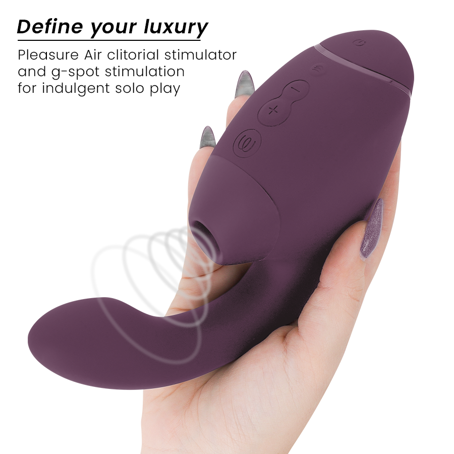 Main aux ongles gris tenant le stimulateur double prune Womanizer de face : embout d'air pulsé clitoridien et tige interne vibrante courbée en silicone doux.