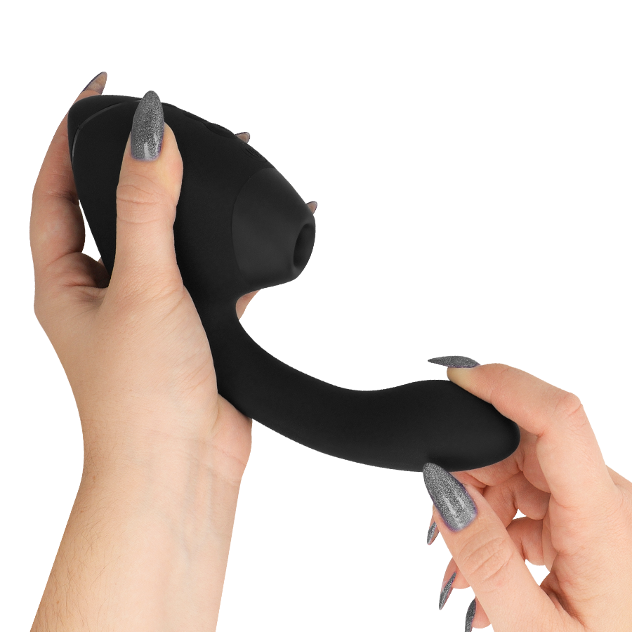 Main tenant le stimulateur double noir Womanizer, embout de succion orienté vers le haut et bras vibrant interne lisse, surface silicone mate sans relief anatomique.