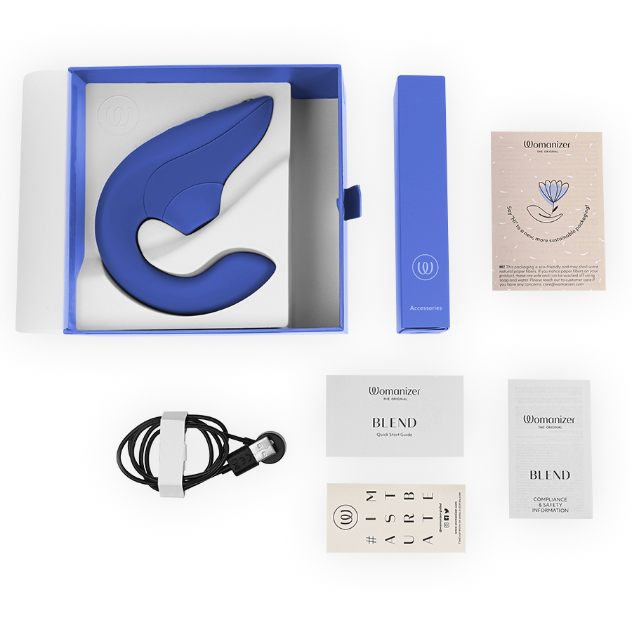 Coffret bleu Womanizer ouvert avec le stimulateur lapin dans son logement, câble de charge magnétique, notice et carte, disposés à plat sur fond blanc.