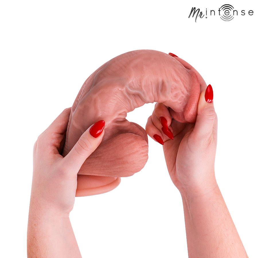 Gode realiste Intense en silicone chair plie en U par deux mains aux ongles rouges, illustrant la souplesse de la matiere veinee et du gland.