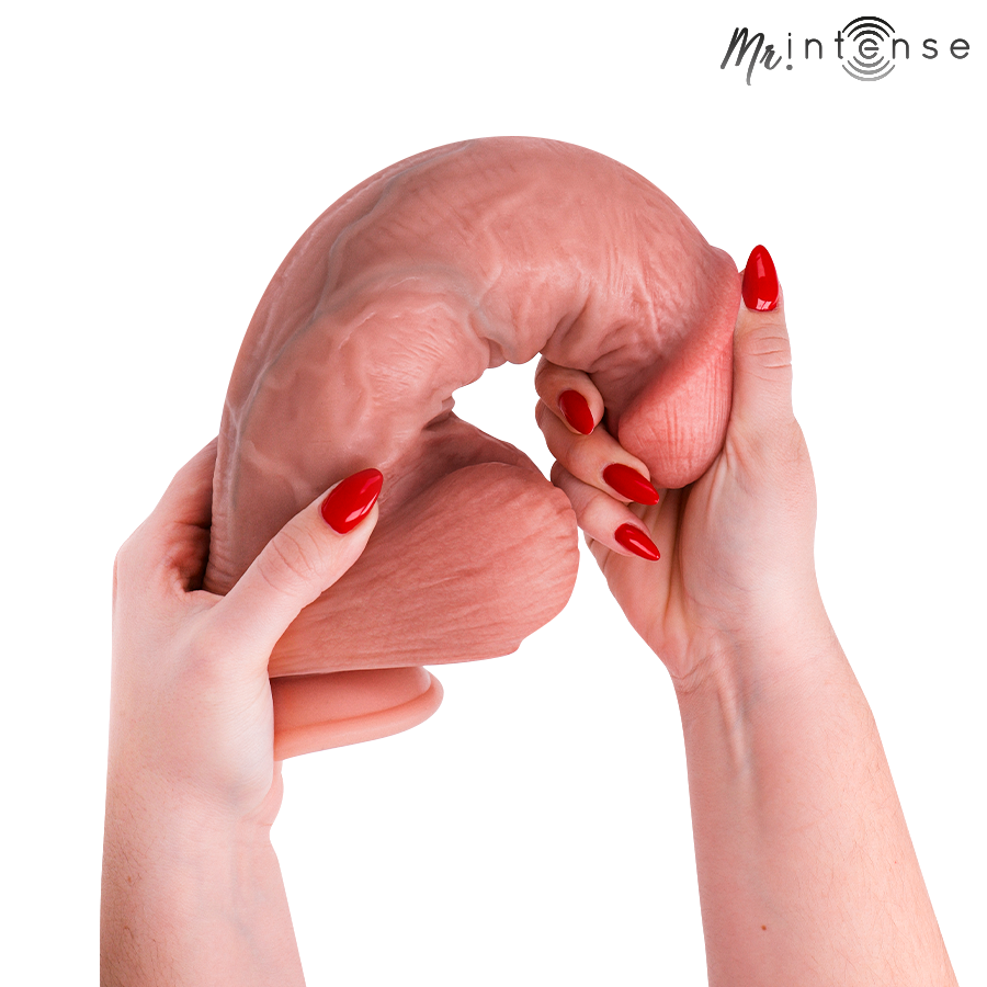 Gode realiste Intense en silicone chair plie en boucle par deux mains aux ongles rouges, demontrant la flexibilite extreme de la matiere veinee.