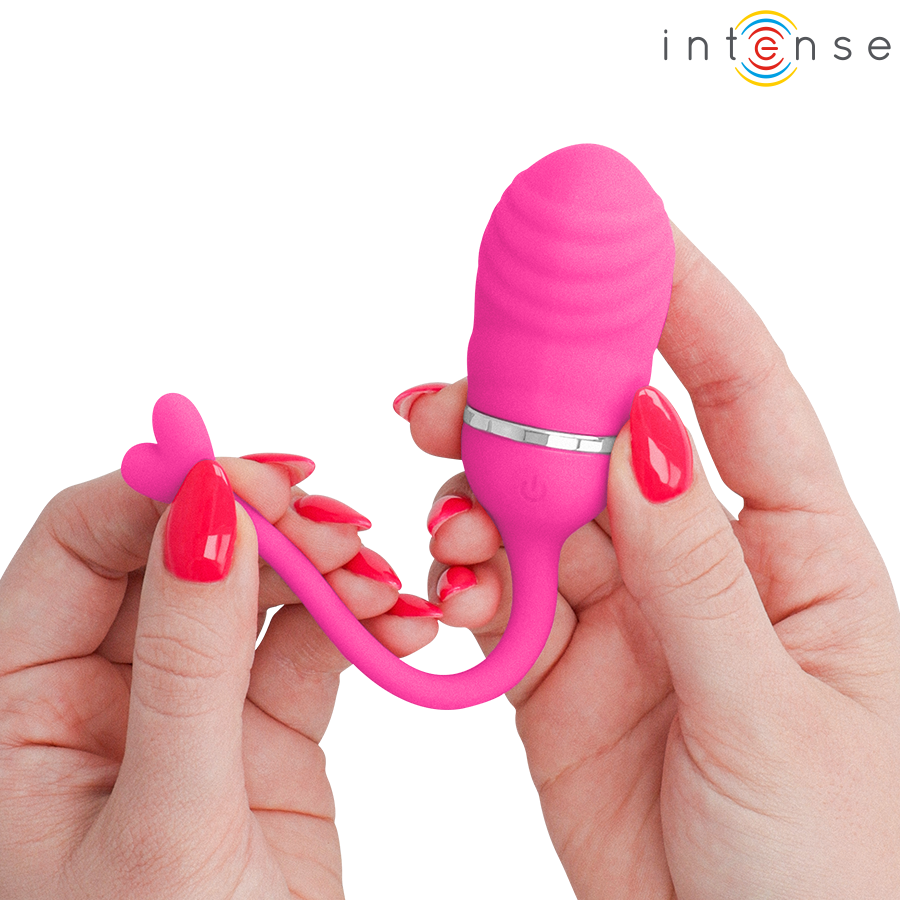 Sookie œuf vibrant rose — tenu à deux mains, gros plan sur l'extrémité en forme de cœur de la queue de récupération, ongles rouges