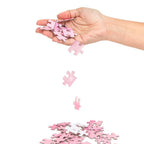Jeu de casse-tête 'Sexxxzzle' — main laissant tomber des pièces de puzzle roses au-dessus d'un tas de pièces