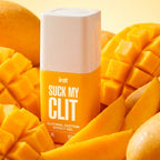 Suck My Clit gel effet succion mangue tropicale — flacon posé au milieu de morceaux de mangue fraîche