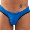 Slip bleu vif vu de face en gros plan sur l'entrejambe, liserés noirs sur les côtés, tatouage de serpent sur la hanche du modèle.