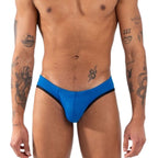 Slip bleu vif vu de face, plan plus large incluant le buste et les avant-bras tatoués.