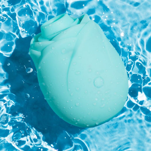 Stimulateur clitoridien Rose ROMP vert d eau pose dans l eau, design fleur de rose en silicone etanche, gouttes visibles soulignant la resistance a l eau du produit