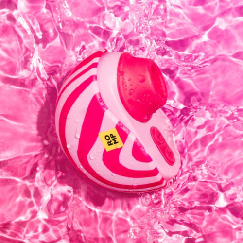 Stimulateur clitoridien par succion ROMP flottant sur une eau rose : coque spiralee et tete d'aspiration corail, demonstration de l'etancheite de ce jouet a air pulse waterproof.