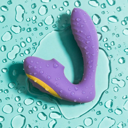 Stimulateur deux-en-un Reverb ROMP violet pose sur surface mouillee turquoise, illustrant l'etancheite et la combinaison point G plus succion clitoridienne.