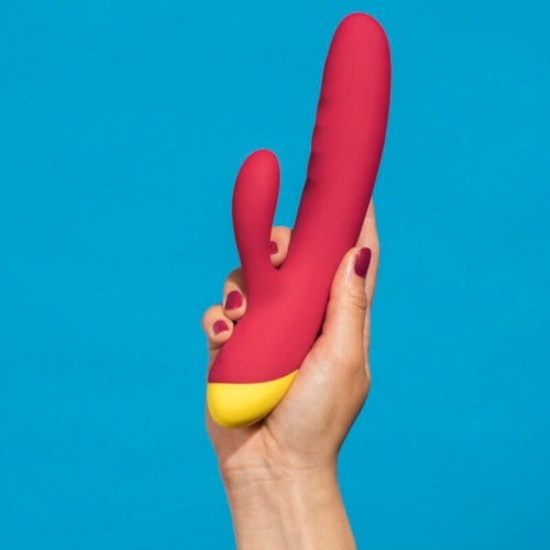 Main tenant le vibromasseur lapin ROMP rouge sur fond bleu, illustrant la taille et la double stimulation clitoridienne et point G en silicone doux.