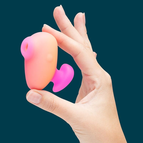 Doigts tenant le mini stimulateur clitoridien a succion ROMP corail, fond sombre mettant en valeur sa petite taille et son embout d'aspiration en silicone.