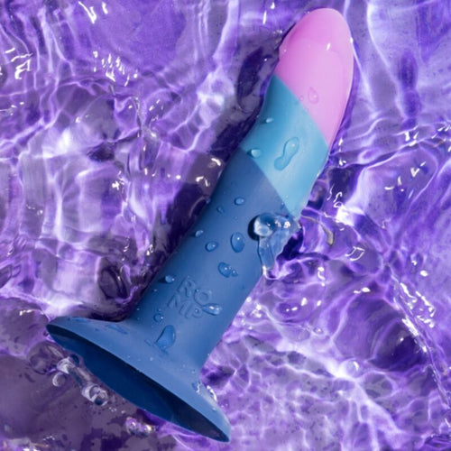 Gode ROMP Piccolo non realiste en silicone tricolore pose sur fond aquatique violet, perles d'eau sur la surface lisse, base ventouse etanche mains libres.