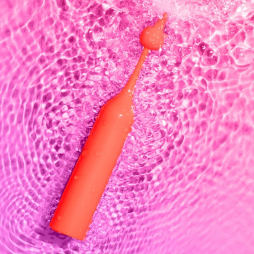 Stimulateur clitoridien Pop ROMP rouge pose dans l'eau sur fond rose, illustrant l'etancheite du silicone doux et ses vibrations haute frequence pour le clitoris.