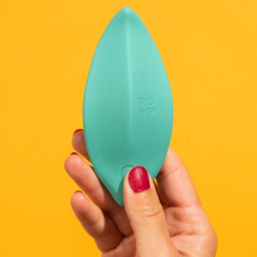 Stimulateur clitoridien Wave ROMP vert tenu entre les doigts sur fond jaune, forme effilee en silicone medical mettant en avant la taille compacte et nomade