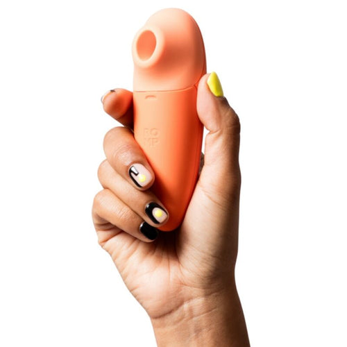 Stimulateur clitoridien Switch X ROMP corail tenu en main, vue de face de la tete d aspiration et de la prise ergonomique, format discret pour une stimulation externe