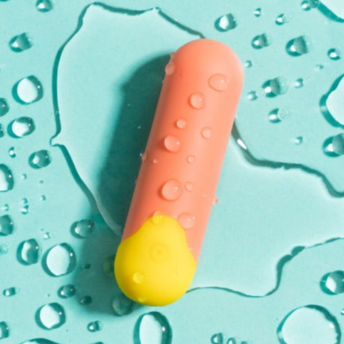 Mini vibromasseur balle Riot ROMP corail pose sur surface mouillee turquoise, illustrant l'etancheite et le format de poche de ce bullet puissant.