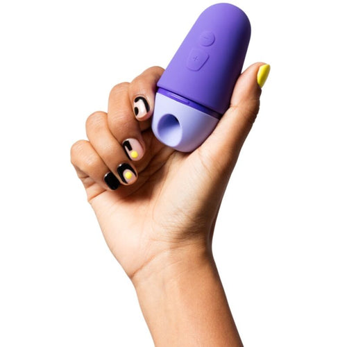 Stimulateur clitoridien ROMP en silicone violet tenu dans une main, montrant la tete a succion et les boutons de commande de ce toy compact rechargeable.
