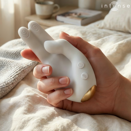 Vibromasseur Jimmy Intense blanc en forme de main tenu dans une main sur un lit clair, deux doigts vibrants a embouts spirales, sextoy clitoridien en situation
