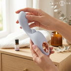 Anya stimulateur multifonctionnel lavande — tenu à deux mains dans une mise en scène cosy avec bougie, huile essentielle et serviette