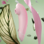 Vue de profil du Womanizer Premium Eco rose, entouré de feuillages sur un fond vert.