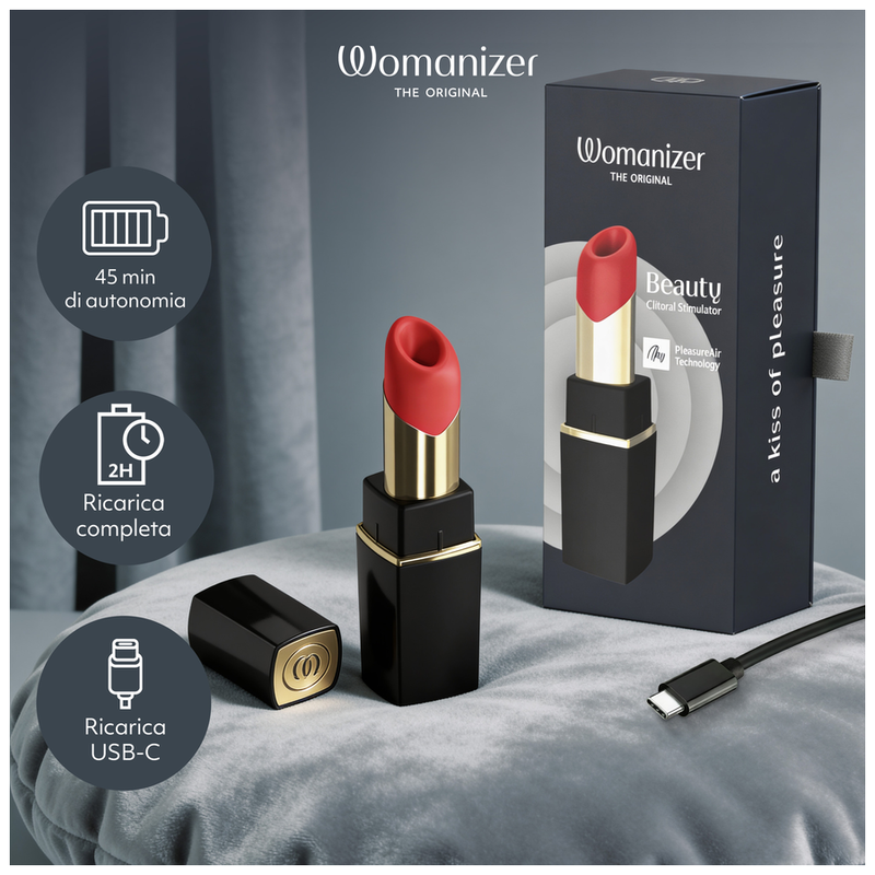 Womanizer Beauty noir et or posé sur un lit, avec son coffret, son capuchon et son câble USB-C.